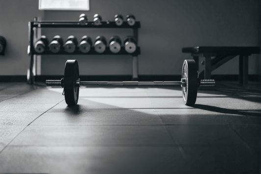 Close-up van halterstang met zwarte schijven op een lichte sportvloer in natuurlijk daglicht.