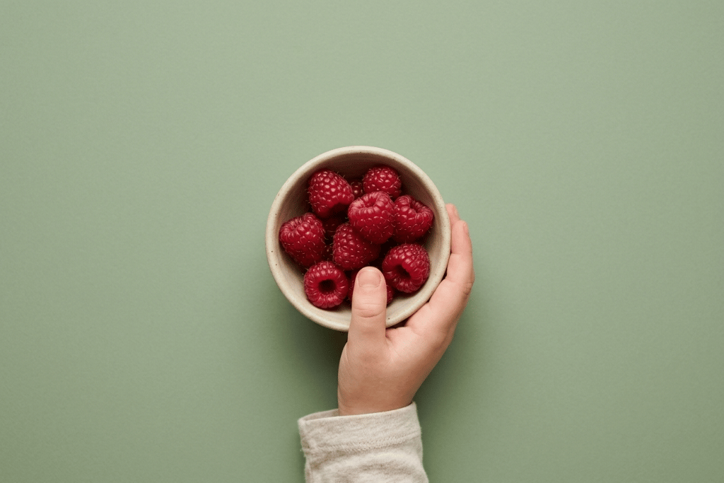 Hand van kind met bakje frambozen